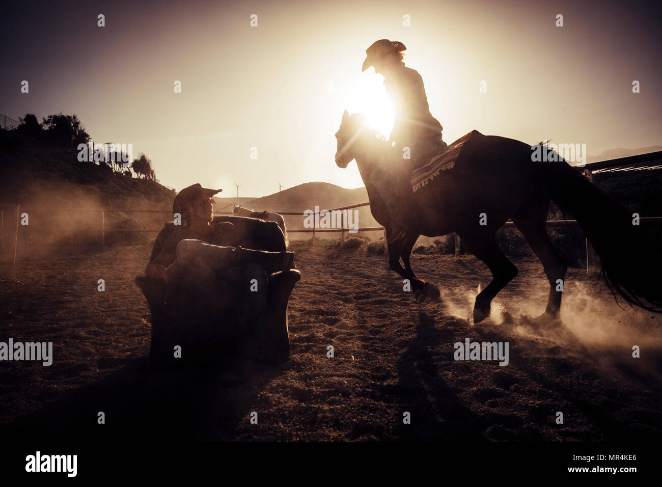 Concepto de héroe dramático y publicidad de imagen estilo cowgirl haciendo polvo a caballo cerca de un vaquero siéntese en una silla en medio de la pista. Foto de stock