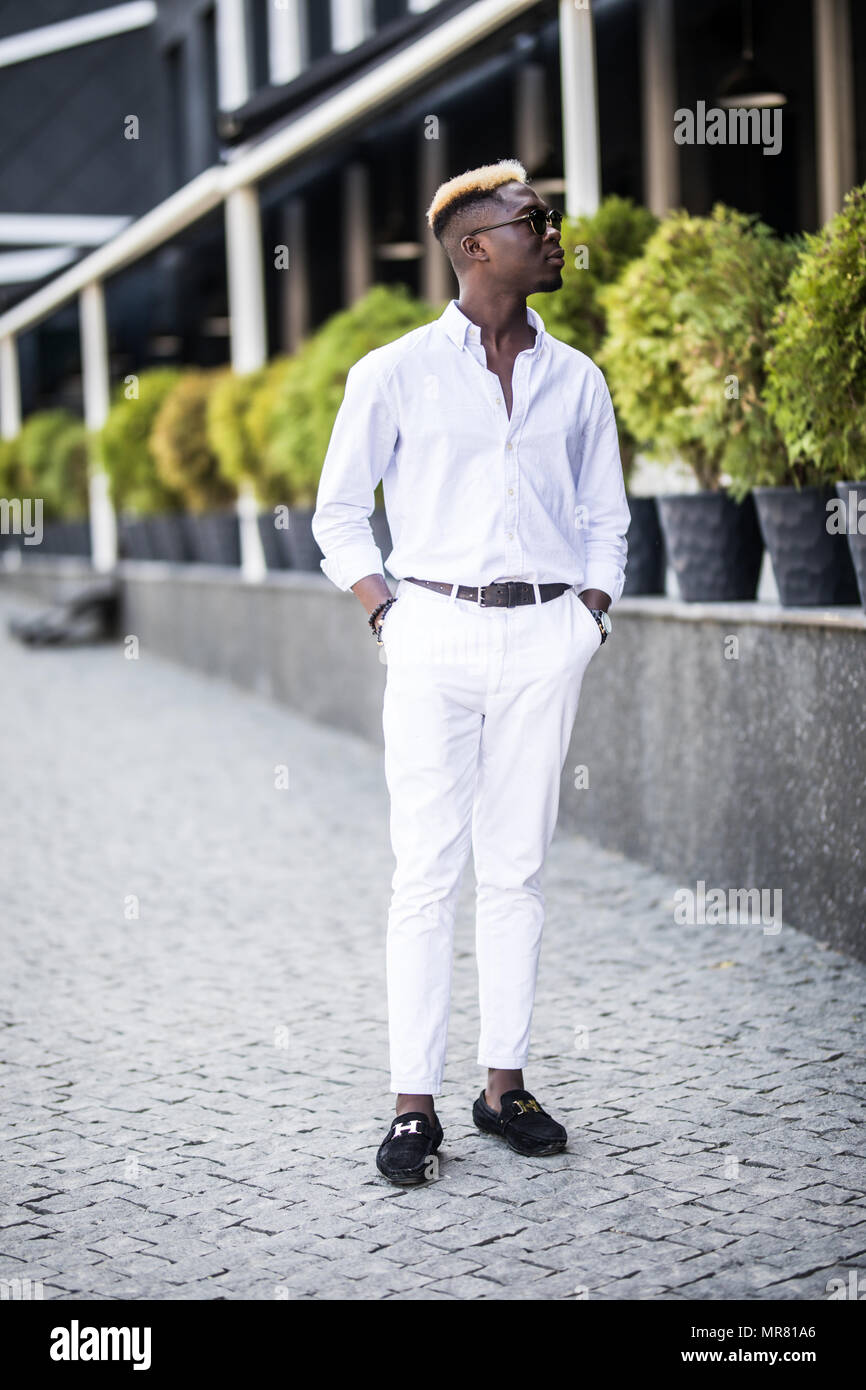 Apuesto hombre de negocios americano Afro vistiendo ropa elegante en la  ciudad moderna se encuentra cerca del edificio Fotografía de stock - Alamy