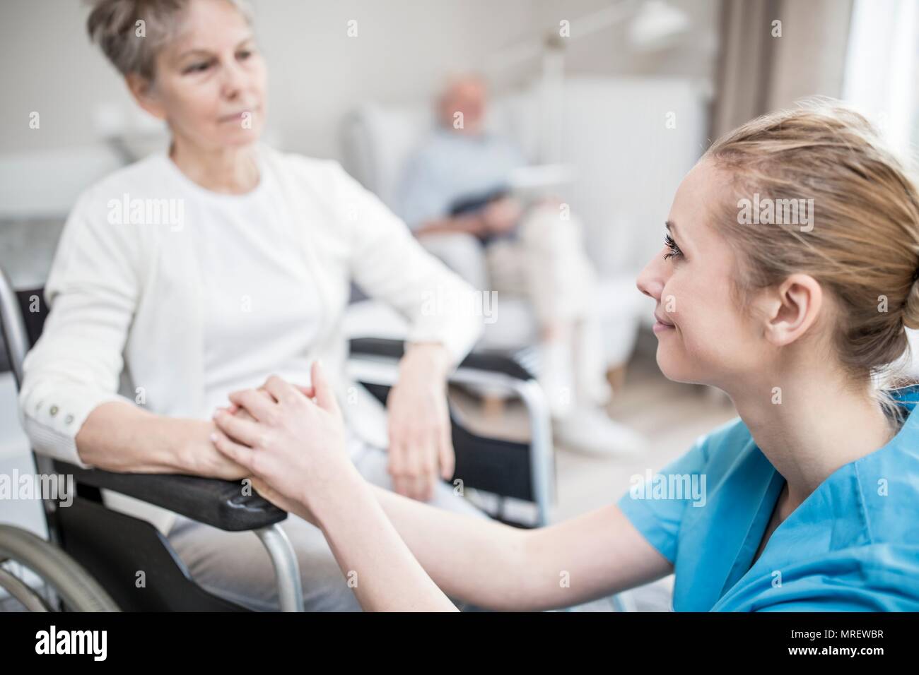 Tranquilizador, trabajador del cuidado de la mujer de más edad en silla de ruedas en el cuidado en casa. Foto de stock