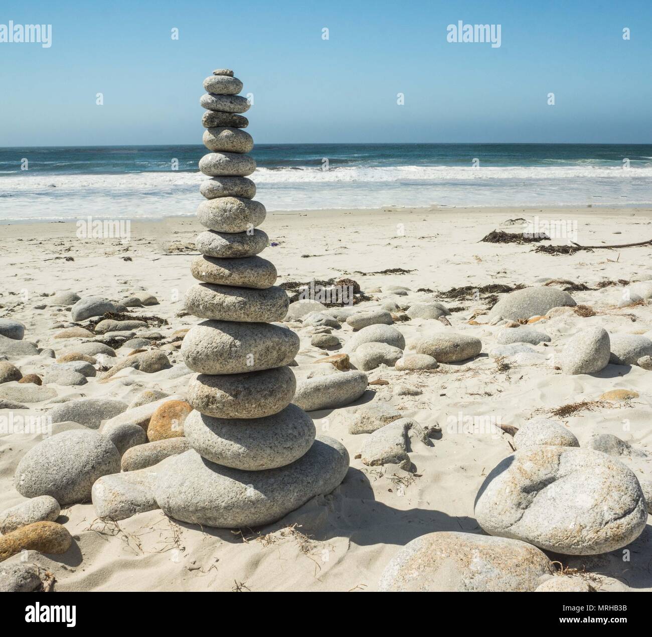 Piedras apiladas en una playa de arena fina por el océano. Foto de stock