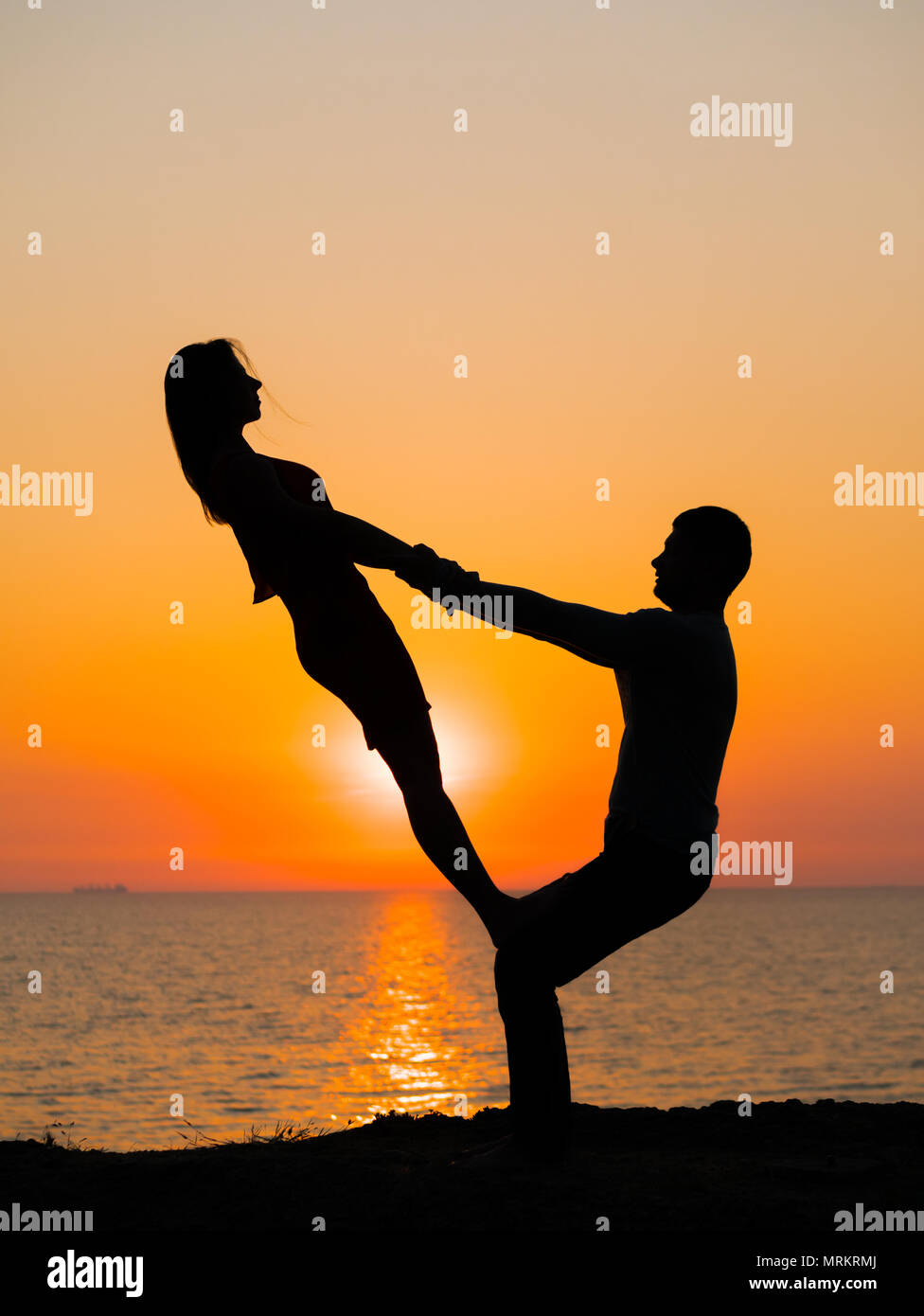 Silueta de la mujer y el hombre joven pareja haciendo yoga en la playa al  atardecer. La meditación. Pareja practicando yoga acro. Ejercicios de  flexibilidad en el fondo de la naturaleza Fotografía