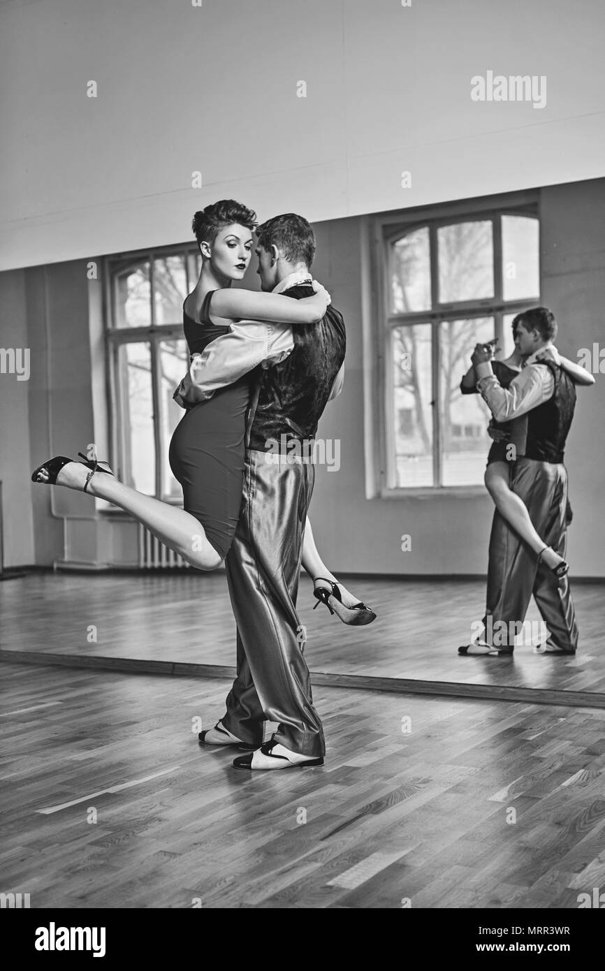 Hermosa pareja bailando tango. mujer joven en vestido rojo y el hombre en  traje practicando en estudio de baile sala de espejo. Copie el espacio  Fotografía de stock - Alamy