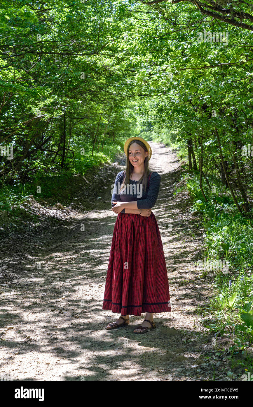 Una chica con una falda roja está en un camino forestal Foto de stock