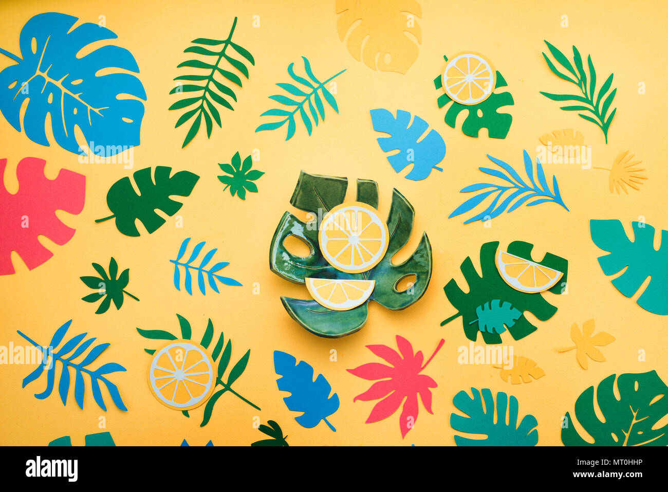 Hoja monstera cerámica en tropical cabezal con naranjas, hojas y frutos patrón sobre un fondo de color amarillo brillante. Colorido laicos plana con recortes de papel. Foto de stock