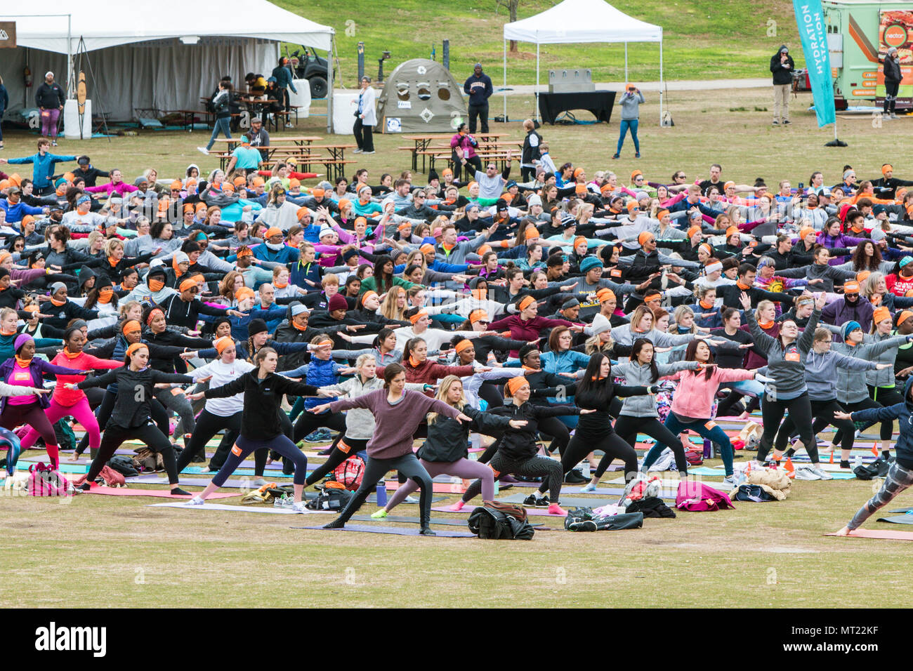 Decenas de personas hacen una versión del guerrero plantean a medida que toman parte en una gran grupo de clase de yoga en el parque Piedmont en Atlanta, GA, el 8 de abril de 2018. Foto de stock