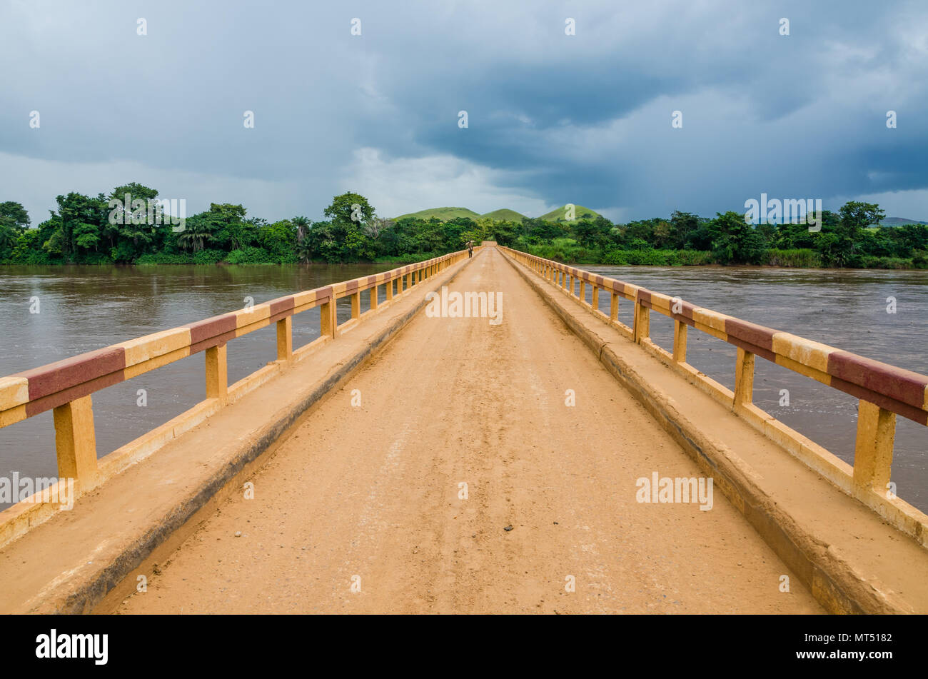 Camino de tierra simple puente sobre el río tropical con dramáticas nubes en la República del Congo, África Foto de stock