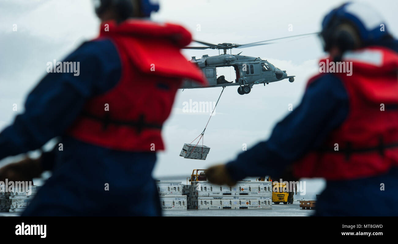 180514-N-OY799-0326 las aguas al sur de Japón (14 de mayo de 2018) un MH-60S Sea Hawk, asignado al comando de Transporte Marítimo Militar (MSC) carga seca/municiones buque USNS César Chávez (T-AKE 14), suministra explosivos como los marineros de cubierta departamento hombre el teléfono y distancia en línea de la cubierta de vuelo a bordo de la Marina desplegadas, el portaviones USS Ronald Reagan (CVN 76), como parte de una reposición en alta mar durante las pruebas de mar. Los civiles no combatientes, con tripulación de barco, operado por la MSC, proporciona el combustible, alimentos, municiones, piezas de repuesto, el correo y otros suministros a los buques de la Marina en todo el mundo. Ronald Reagan, el buque insignia Foto de stock