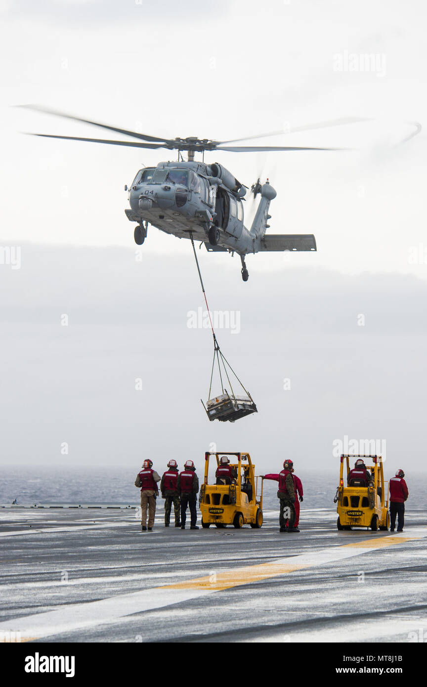 180514-N-OY799-0425 las aguas al sur de Japón (14 de mayo de 2018) Los marineros de armas departamento espera como un MH-60S Sea Hawk, asignado al comando de Transporte Marítimo Militar (MSC) carga seca/municiones buque USNS César Chávez (T-AKE 14), ofrece detonar en la cubierta de vuelo a bordo de la Marina desplegadas, el portaviones USS Ronald Reagan (CVN 76), como parte de una reposición en alta mar durante las pruebas de mar. Los civiles no combatientes, con tripulación de barco, operado por la MSC, proporciona el combustible, alimentos, municiones, piezas de repuesto, el correo y otros suministros a los buques de la Marina en todo el mundo. Ronald Reagan, el buque insignia de transportista Strik Foto de stock