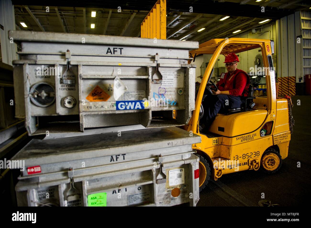 180515-N-OY799-0726 las aguas al sur de Japón (15 de mayo de 2018) la aviación aviador Ordnanceman Gabriel Cabrera, de la Ciudad de Sioux, Iowa, pilas de cajas de municiones en el hangar bay a bordo de la Marina desplegadas, el portaviones USS Ronald Reagan (CVN 76), como parte de una reposición en alta mar con el comando de Transporte Marítimo Militar (MSC) carga seca/municiones buque USNS César Chávez (T-AKE 14), durante las pruebas de mar. Los civiles no combatientes, con tripulación de barco, operado por la MSC, proporciona el combustible, alimentos, municiones, piezas de repuesto, el correo y otros suministros a los buques de la Marina en todo el mundo. Ronald Reagan, el buque insignia de la huelga transportista Foto de stock