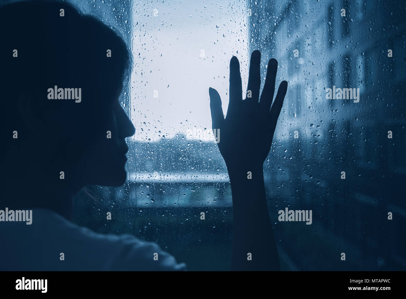 Triste estado de ánimo Depresión solitaria silueta mujer toque ventanas de cristal oscuro día lluvioso fuera Foto de stock