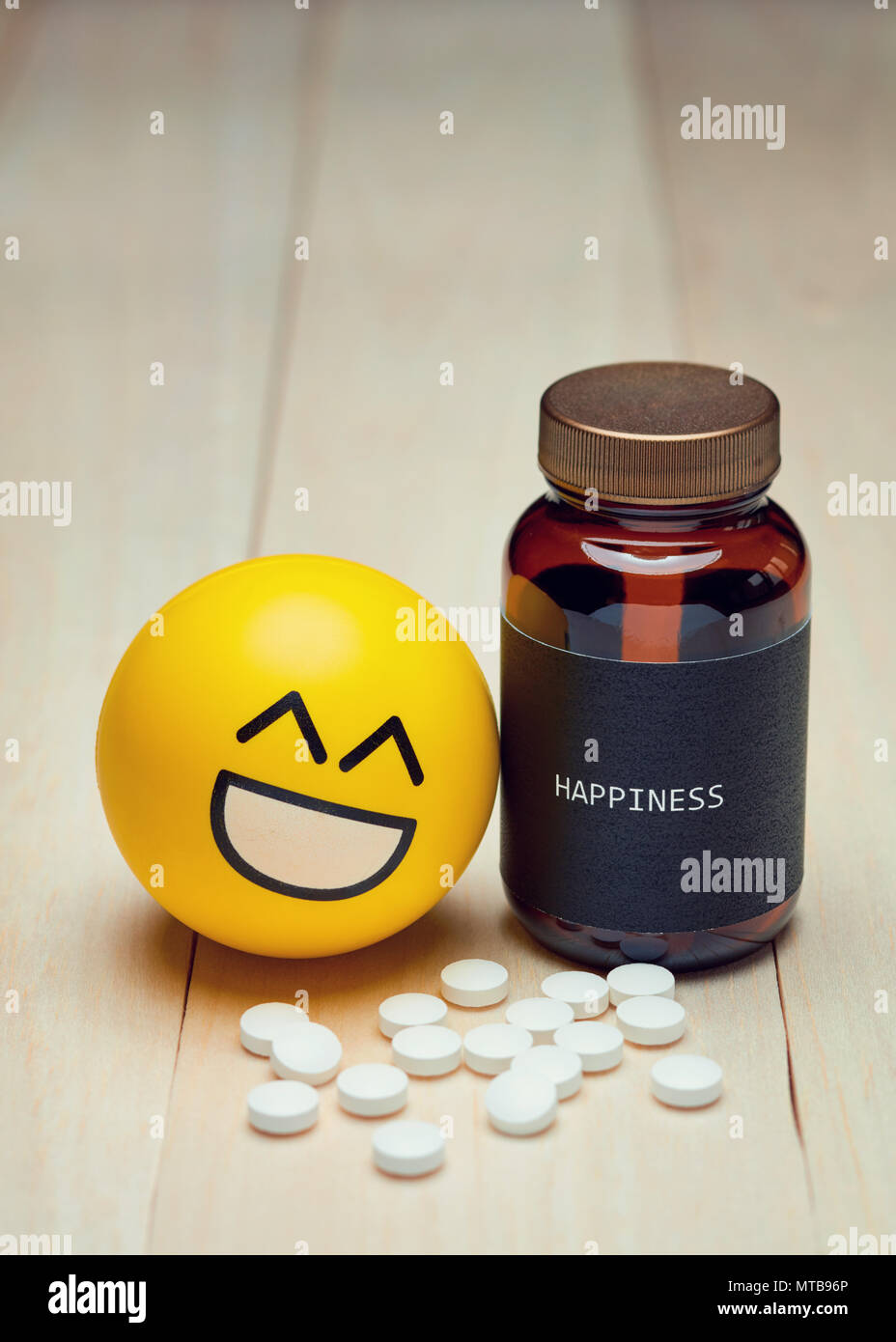 Los anti-depresivos y felicidad. Emoji sonrientes amarillo junto a un contenedor de drogas con una etiqueta negra escrita sobre la felicidad. Pastillas de color blanco sobre la mesa. Foto de stock