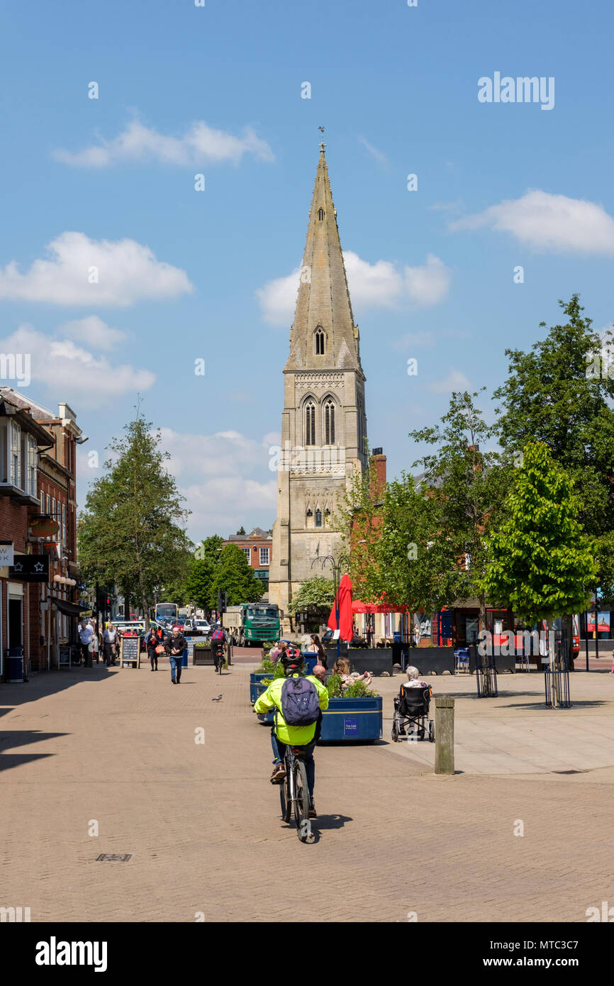 Ciclista de la chaqueta de alta visibilidad y la gente disfrutando del sol en la plaza del mercado. Market Harborough, una ciudad de mercado en Leicestershire, Inglaterra Foto de stock