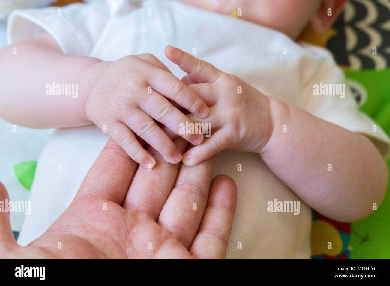 Bebe aguantando la mano de padres adultos, mostrando un bono táctiles, afecto y confianza, dando al niño un sentido de comodidad, seguridad y cercanía Foto de stock