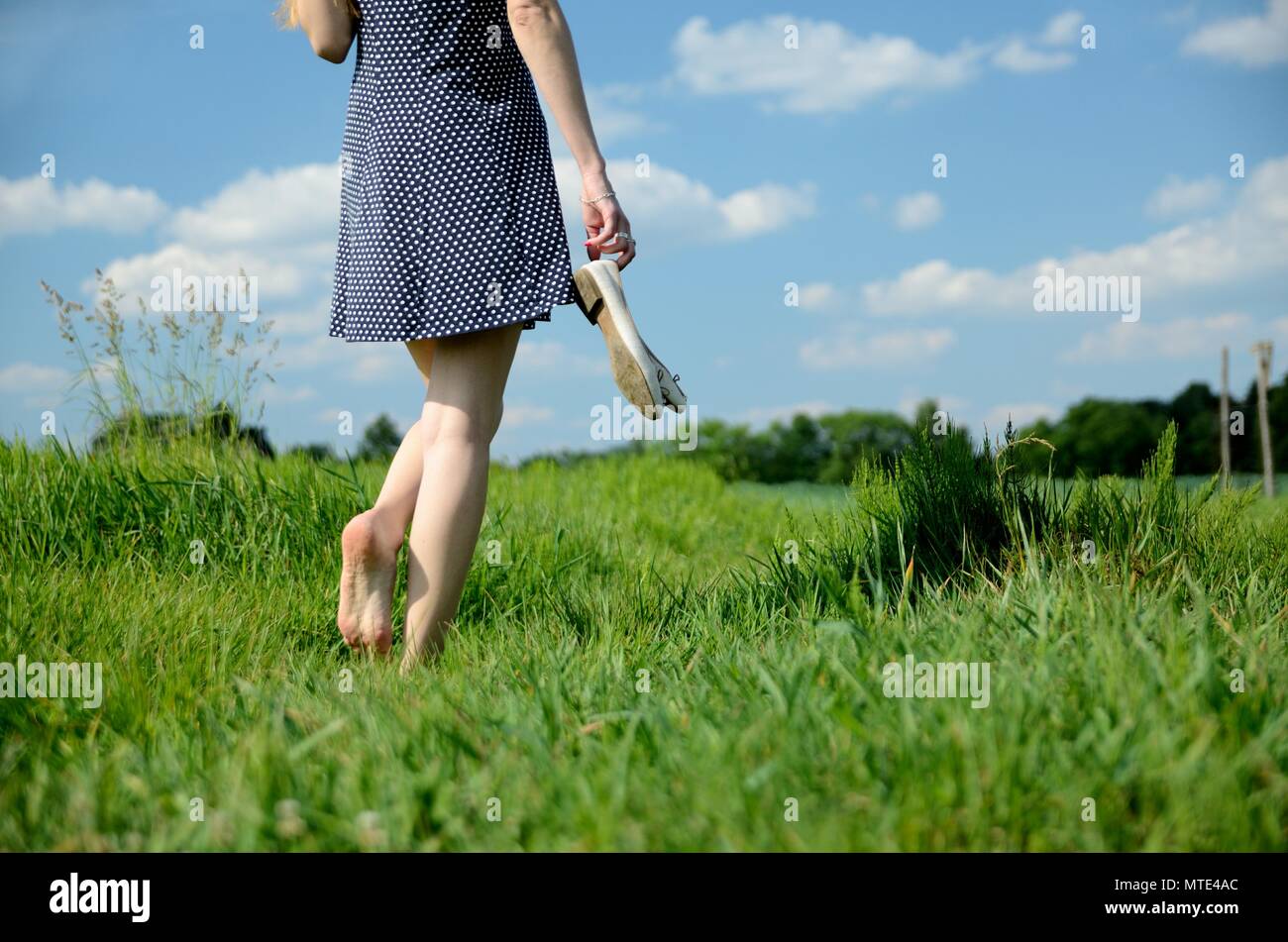 Una niña de 10 años con un vestido azul sentada en un campo de hierba y  flores, piernas largas y desnudas, descalza