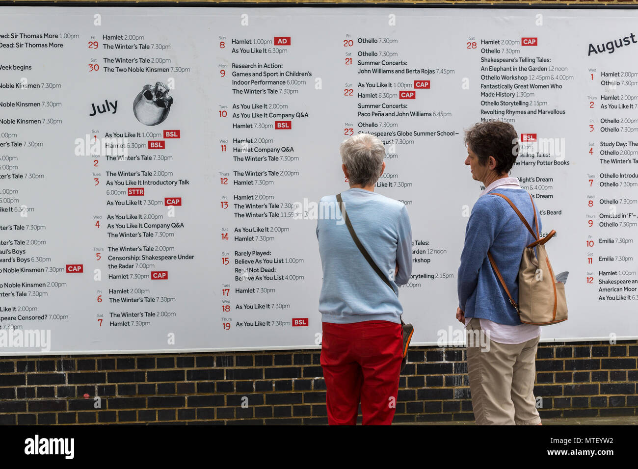 Dos mujeres mirando el calendario de juegos y actuaciones en la pared de Shakespeare's Globe Theatre de Londres Foto de stock
