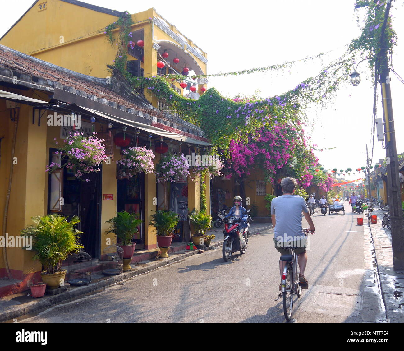 HOI AN, Vietnam - 20 DE MARZO DE 2018: Parte posterior de un hombre montando bicicleta y chica con máscara de panda en moto muy temprano en la mañana en Hoi An Foto de stock