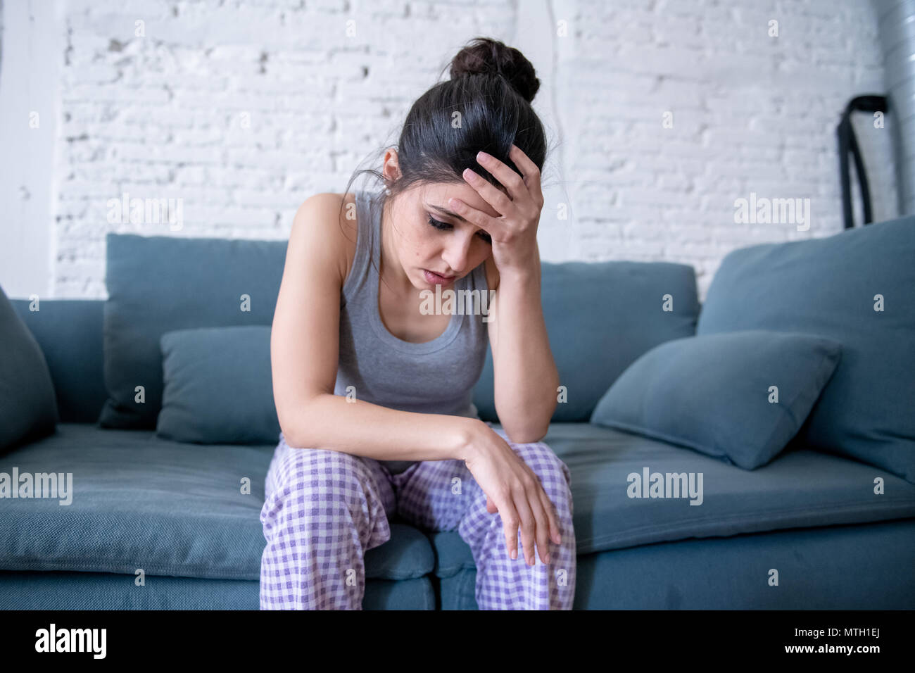 Hermosa latina pisado solitaria mujer mirando por sentimientos de tristeza, dolor, sufrimiento en casa en su sofá. Crisis, depresión y salud mental concepto Foto de stock