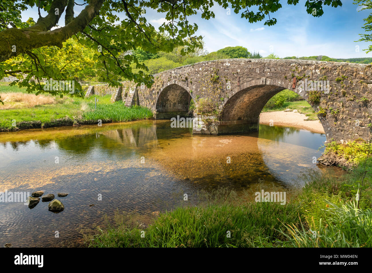 En una cálida tarde de verano, el East Dart River escurre bajo el hermoso puente construido en granito en dos puentes en el parque nacional de Dartmoor. Foto de stock