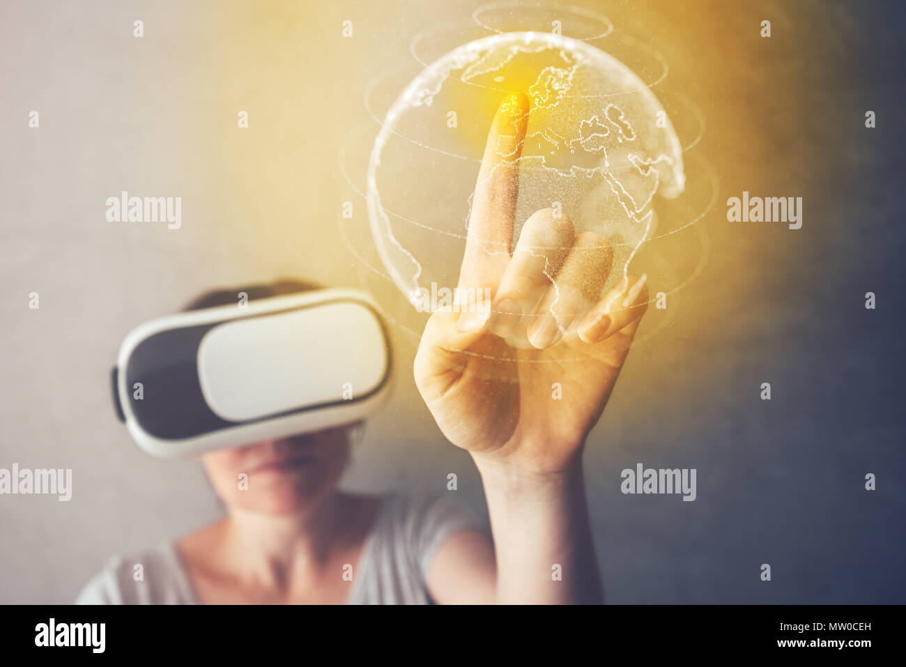 Mujer inmerso en la realidad virtual apuntando a Gran Bretaña en el mapa del mundo, persona de sexo femenino mediante modernos auriculares VR para disfrutar de contenido multimedia en 3D Foto de stock