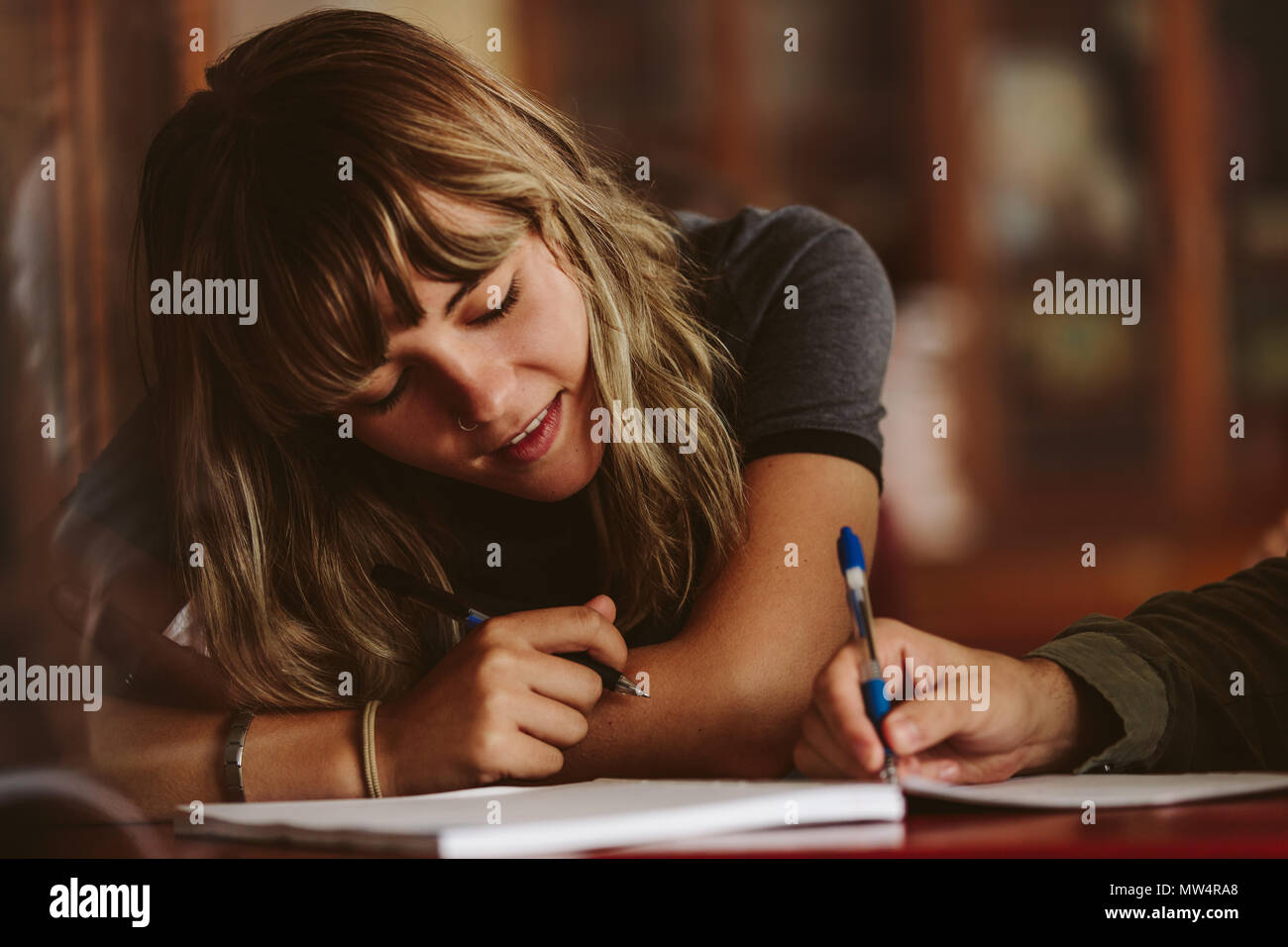 Estudiante femenina mirando a compañero de clase escribiendo en su libro. estudiantes universitarios que estudian en el aula. Foto de stock