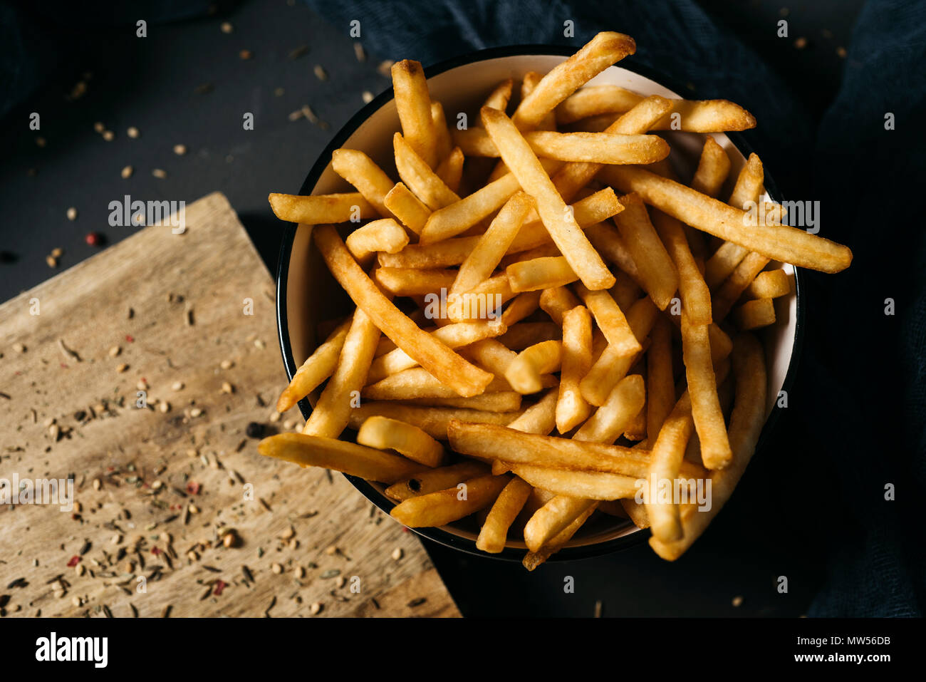 Un alto ángulo de disparo de algunas apetitosas papas fritas servidas en un cuenco de cerámica blanca, colocados sobre una mesa de madera rústica gris oscuro Foto de stock