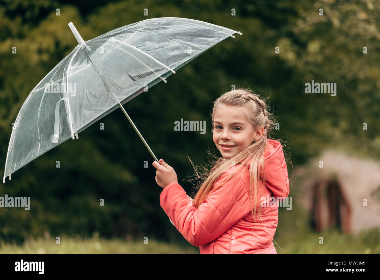 Adorable pequeño niño sosteniendo paraguas y sonriendo a la cámara en otoño park Foto de stock
