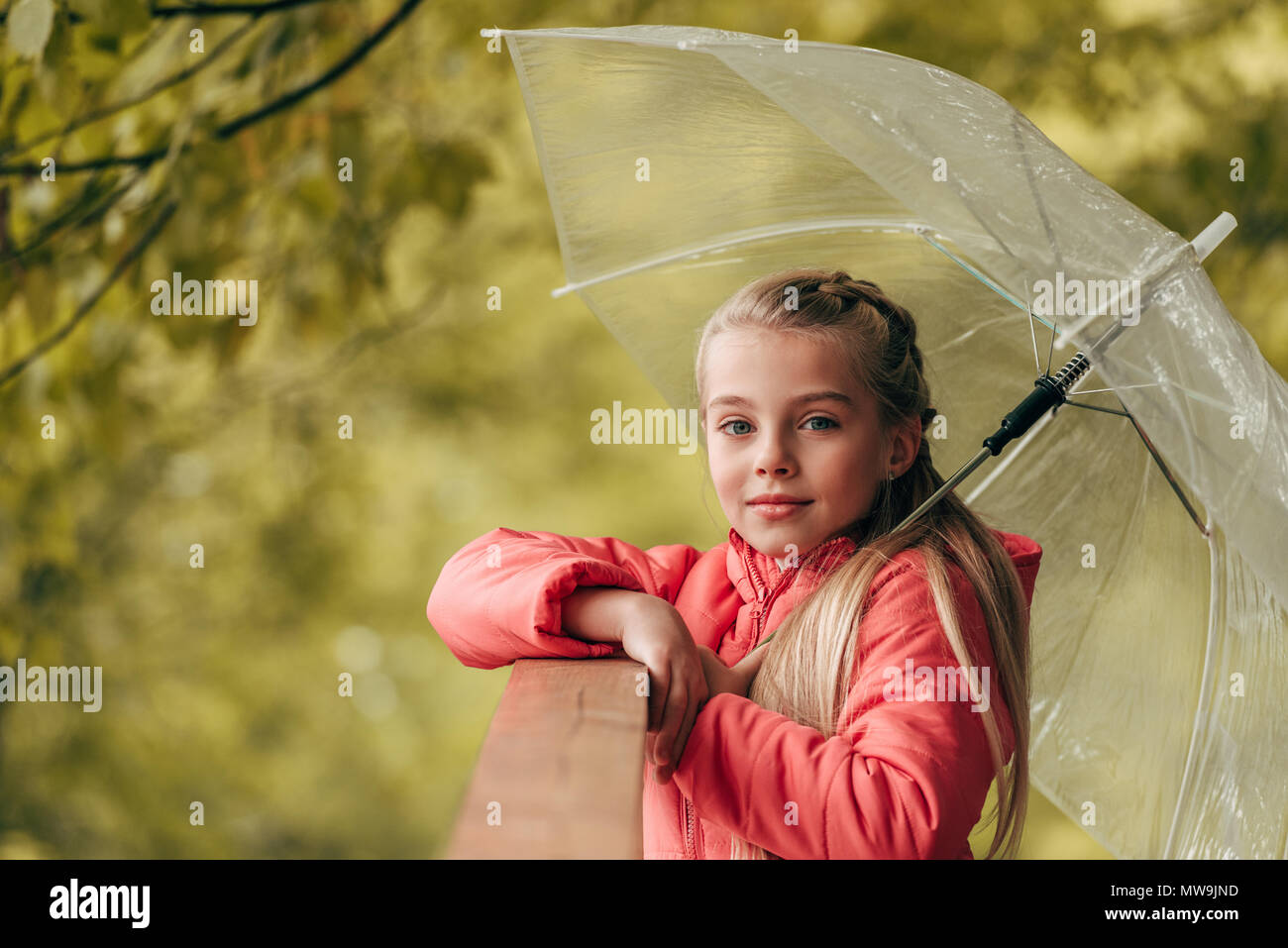 Cute little niño sosteniendo paraguas y mirando a la cámara en otoño park Foto de stock