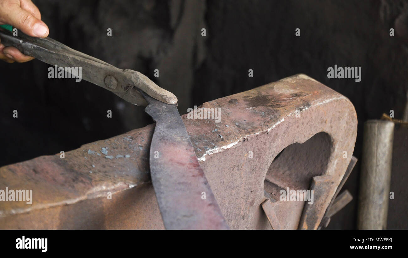 El trabajo de los metales con martillo de herrero sobre el yunque en la  fragua. martillo de forja de hierro caliente en el yunque. Los herreros  hacen machete. Manos de los Smith