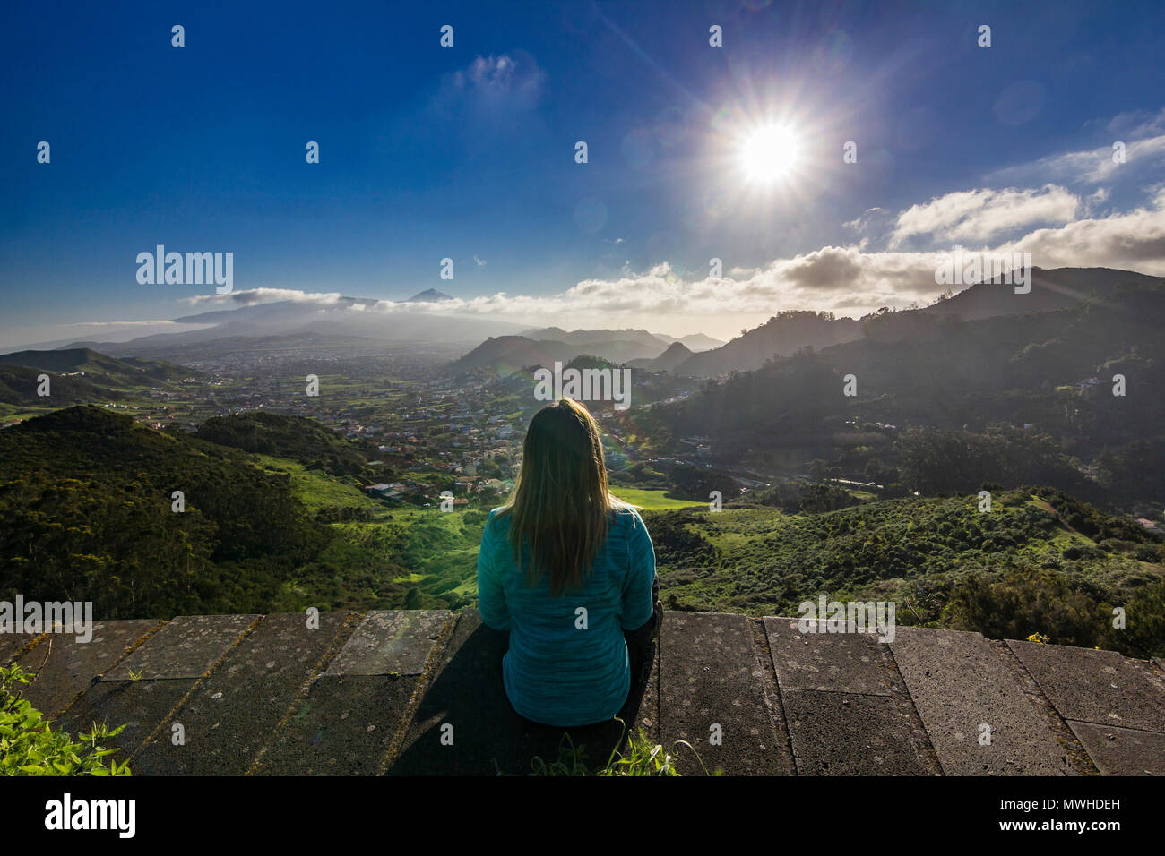 Chica sentada y mirando en colorido atardecer en Tenerife con vista al volcán Teide y aldeas Foto de stock