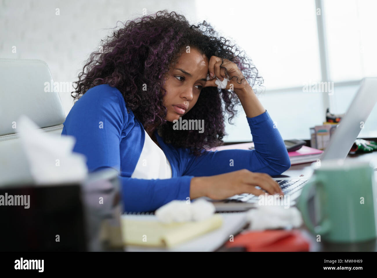 Enfermos African American Girl trabaja desde la oficina en casa. Malos joven negra con frío, sentado en un escritorio con ordenador portátil y estornudos de alergia. Foto de stock