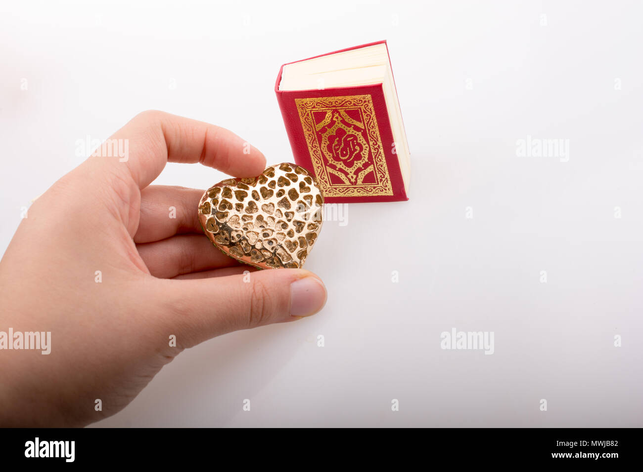 Mano que tiene forma de corazón y libro sagrado islámico Corán Foto de stock