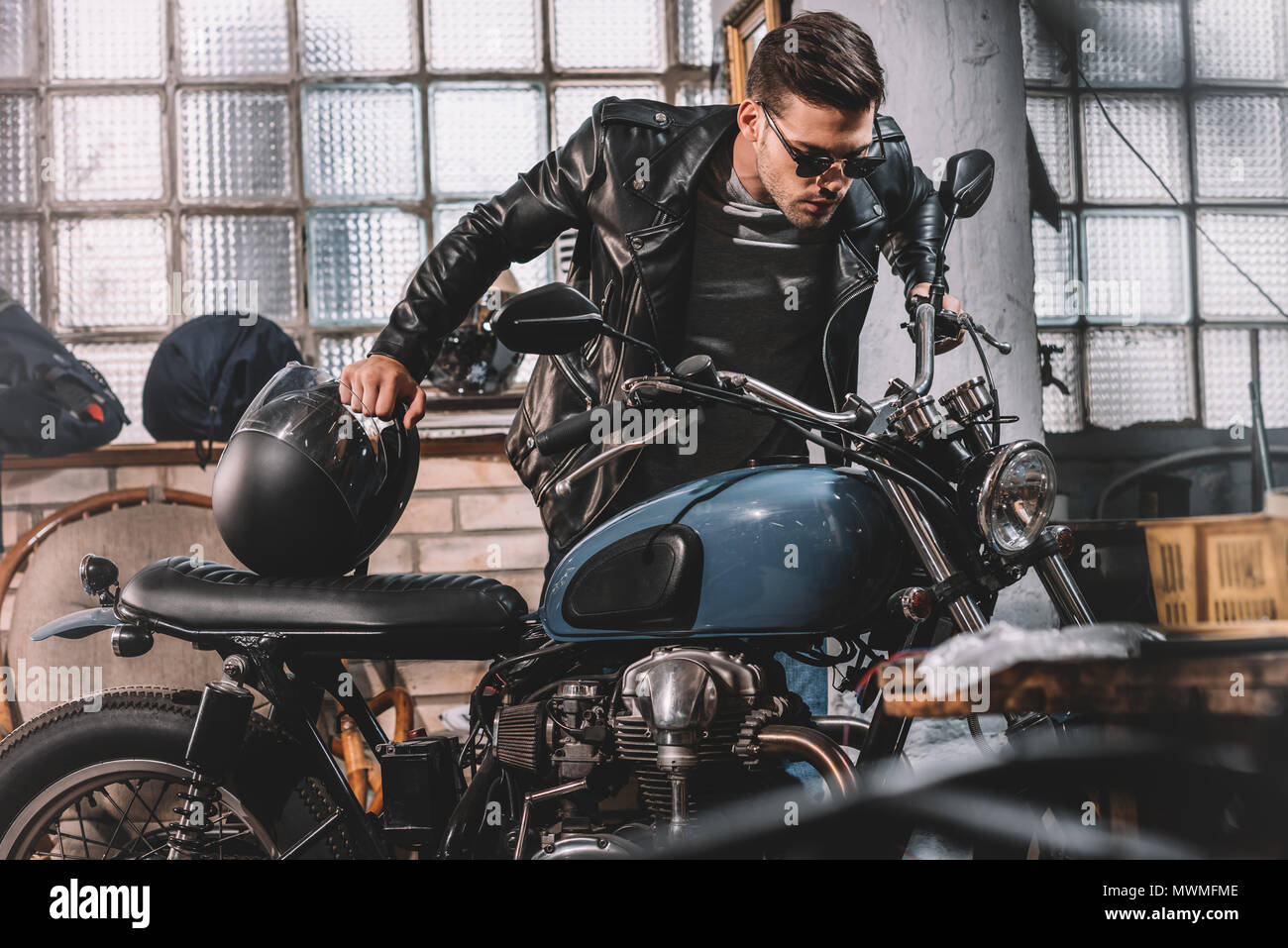 Joven apuesto biker en la chaqueta de cuero negro con moto clásica en el  taller Fotografía de stock - Alamy