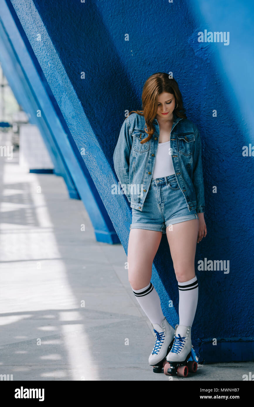 Elegante mujer en jeans ropa, calcetines altos y retro patines inclinarse  sobre pared azul Fotografía de stock - Alamy