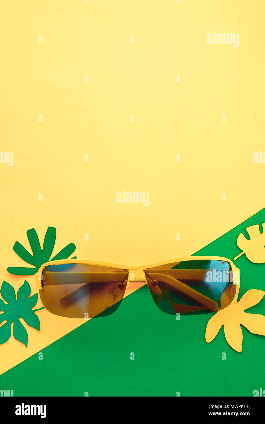 Gafas de sol sobre un fondo de color amarillo brillante con hojas tropicales verdes y amarillos. Piso soleado de verano sentar con espacio de copia. Foto de stock