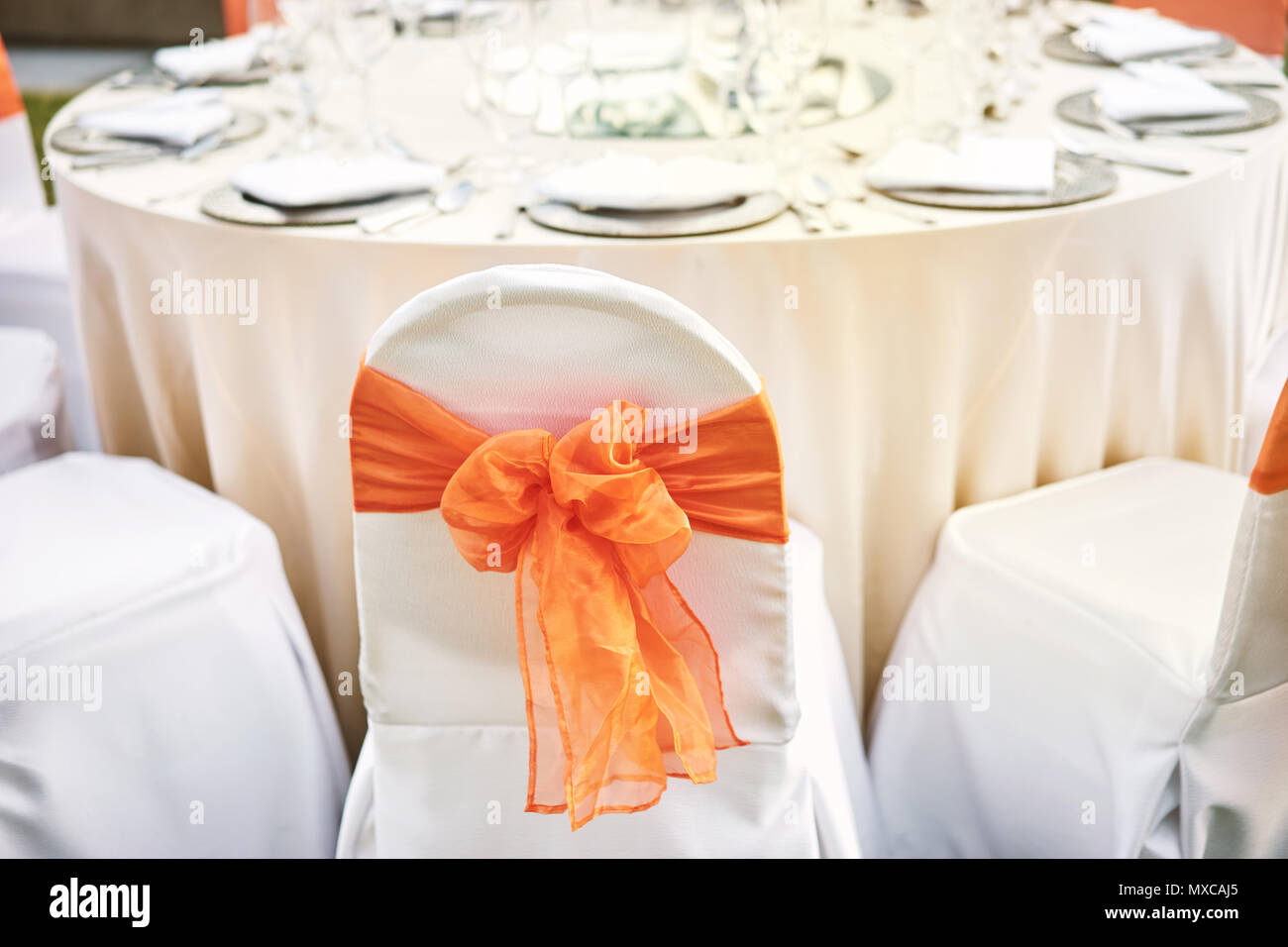 La recepción de la boda mesa con sillas de cubierta blanca de spandex con guillotina de organza naranja Foto de stock