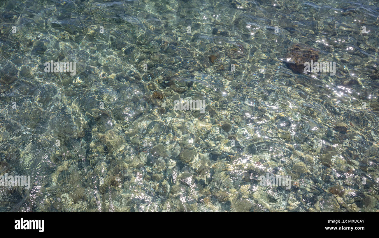 Crystal Clear superficial del agua de mar azul, fondo de guijarros en el lecho marino Foto de stock