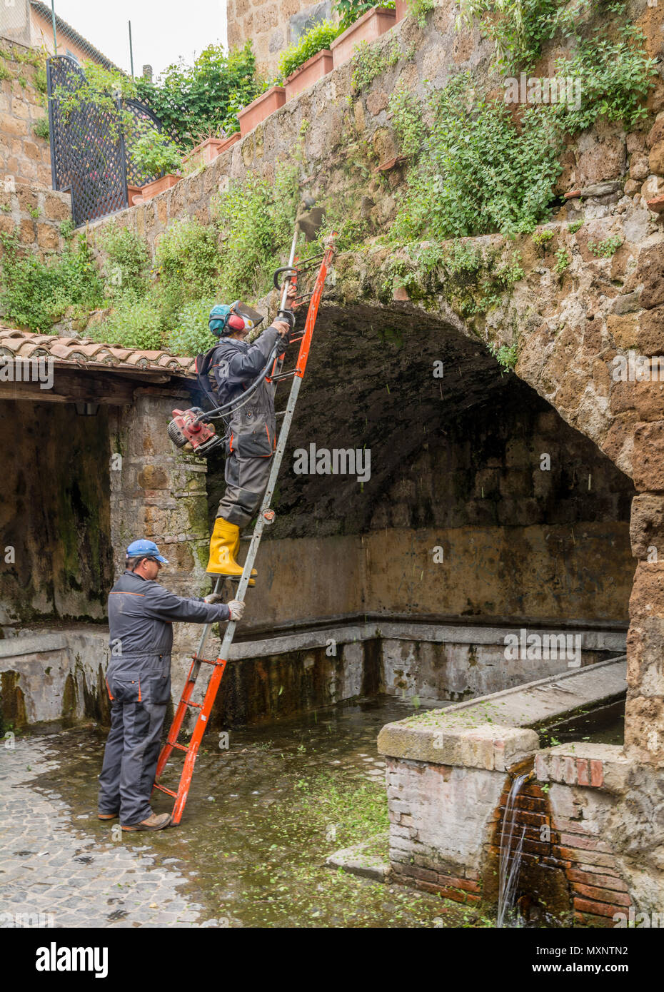 Tuscania (Viterbo), Italia - Mayo 2, 2018: usando strimmer jardinero municipal en un sitio arqueológico en Tuscania, Italia Foto de stock