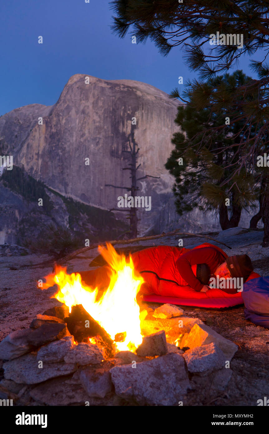 Mujer en el saco de dormir por fuego de campamento en Yosemite camping en  el país alto con fuego de campamento y Half Dome Fotografía de stock - Alamy