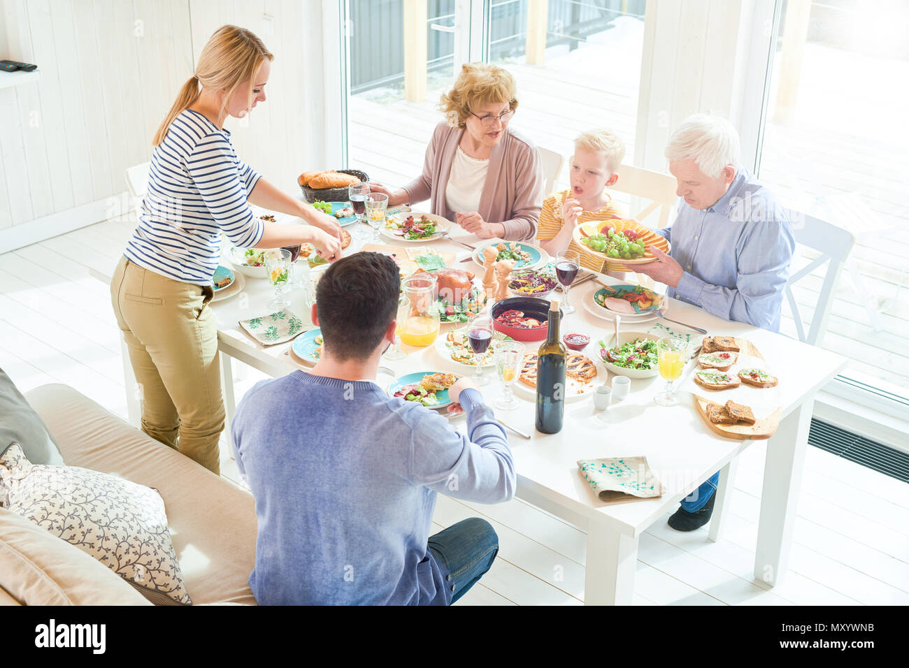 Retrato de dos generaciones de la familia feliz de disfrutar de una cena juntos sentados en la mesa festiva con deliciosos platos durante la celebración navideña en sunli Foto de stock