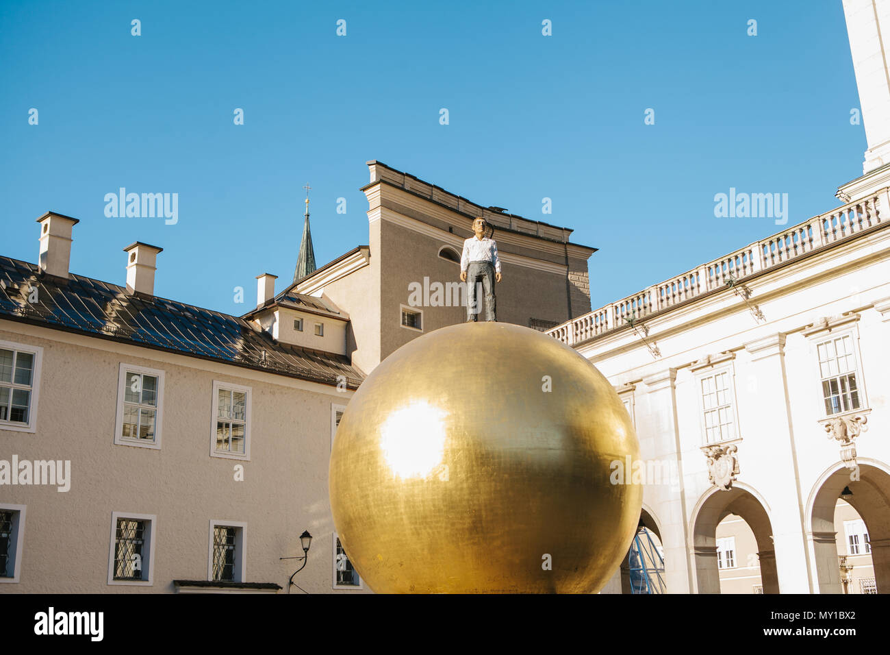 Austria, Salzburgo - 01. 01. 2017. Vista de la bola dorada estatua con hombre en traje formal en la parte superior coloca en la plaza de la ciudad en la luz del sol Foto de stock