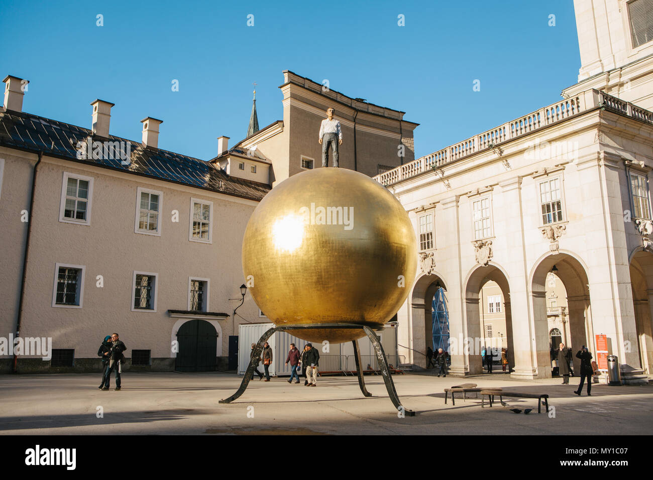 Austria, Salzburgo - 01. 01. 2017. Vista de la bola dorada estatua con hombre en traje formal en la parte superior coloca en la plaza de la ciudad en la luz del sol Foto de stock