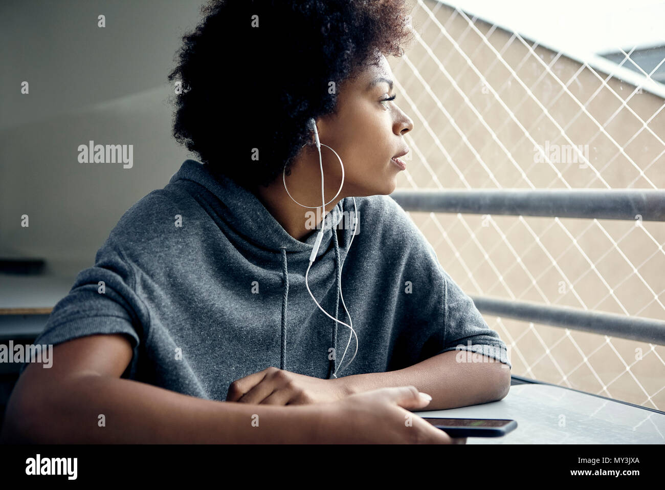 Mujer joven escuchando auriculares y mirando por la ventana Foto de stock