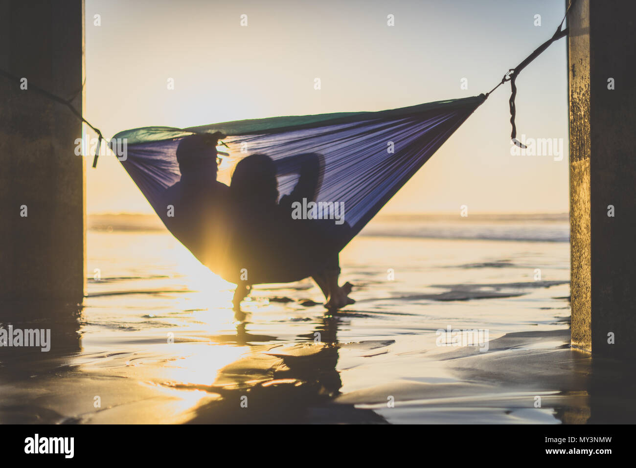 Silueta de pareja mirando el atardecer en la playa en una hamaca Foto de stock