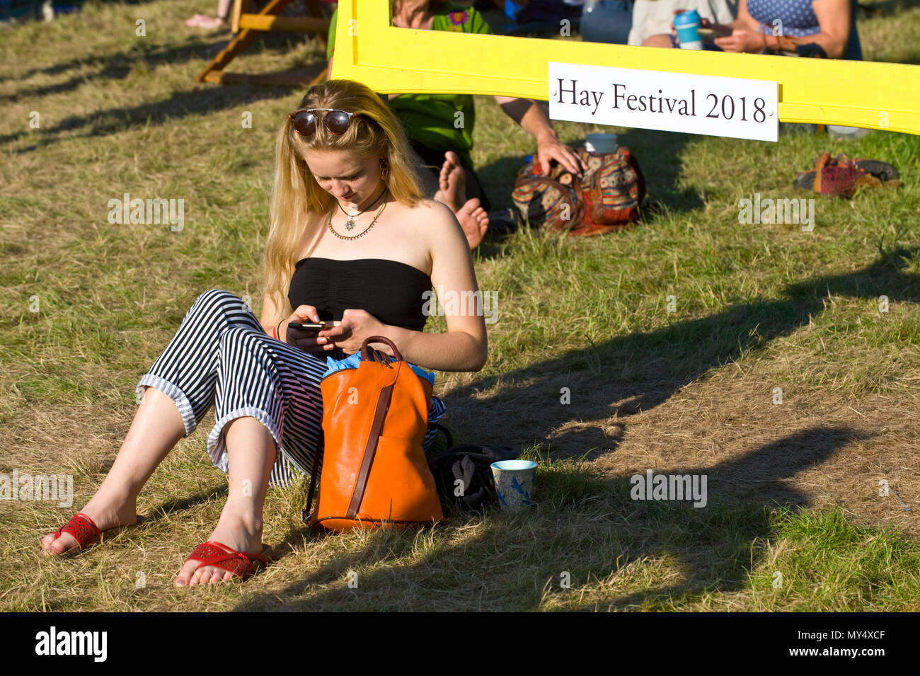 Mujer usando el smartphone en el césped para sentarse en el jardín en 2018 FESTIVAL DE HENO HENO-on-Wye Gales Powys UK Foto de stock
