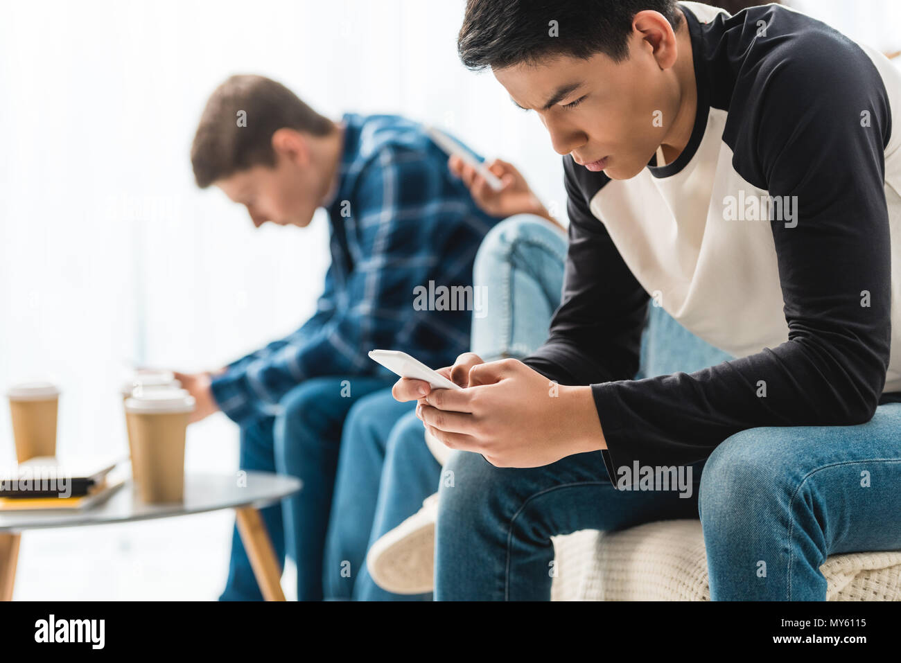 Tres graves adolescentes sentados con los smartphones Foto de stock