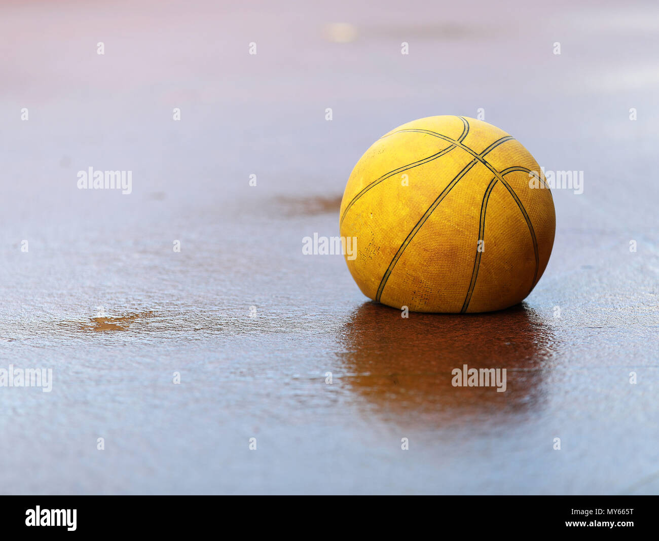 Un desinflado plana viejo cansado amarillo basket ball en el concreto húmedo el suelo. Concepto de sensación de piso, mala mala lluvioso, cansados, enfermos o necesitan ayuda. Foto de stock