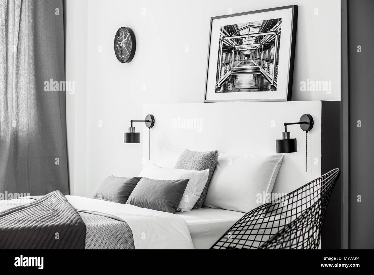 Negro sobre blanco reloj de pared junto a un cartel encima de la cama en habitación sencilla con luces interiores Foto de stock