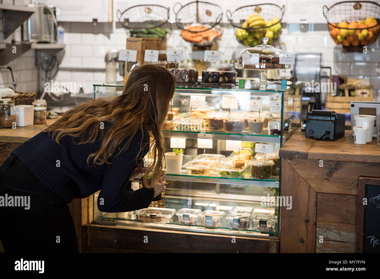 Mujer joven en busca de alimentos frescos vitrina en cafe Foto de stock
