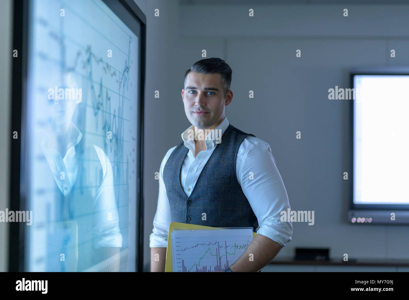 Retrato de joven empresario con pantalla interactiva con gráficos y diagramas en reunión de negocios Foto de stock