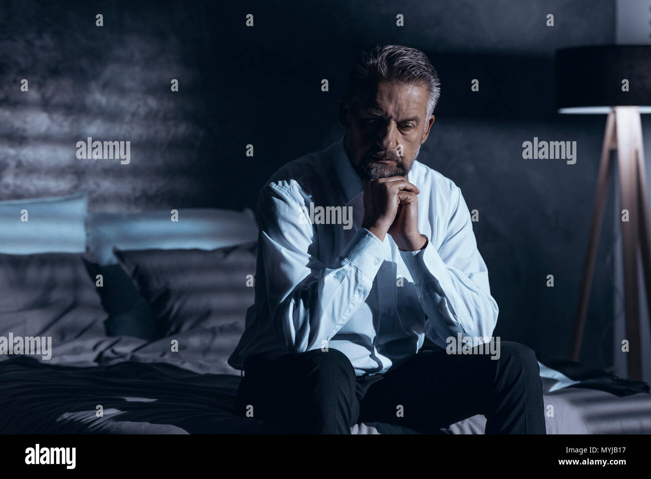 Estresado y deprimido hombre sentado solo en la oscuridad con un problema Foto de stock